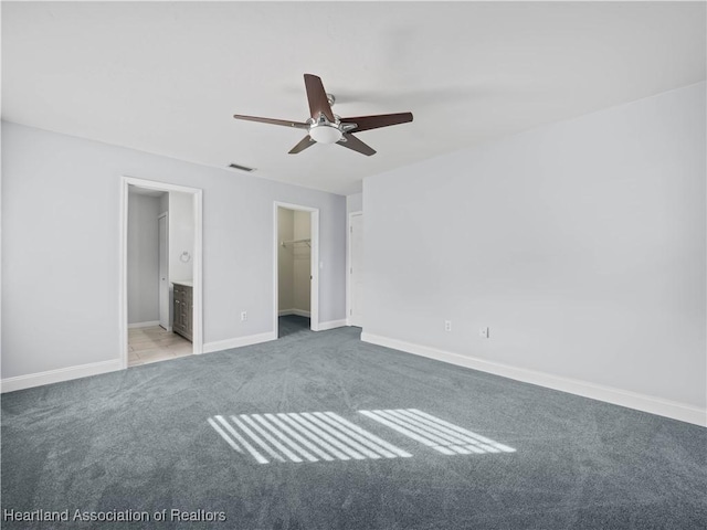 unfurnished bedroom featuring light carpet, ensuite bathroom, a walk in closet, ceiling fan, and a closet