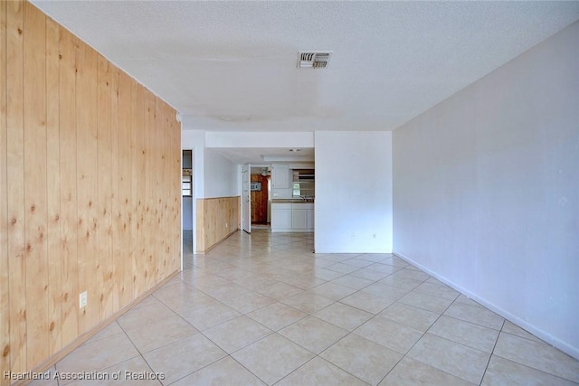 unfurnished room with light tile patterned flooring, a wainscoted wall, a textured ceiling, visible vents, and wood walls