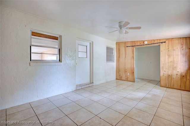 unfurnished room featuring light tile patterned flooring, ceiling fan, a textured wall, and wood walls