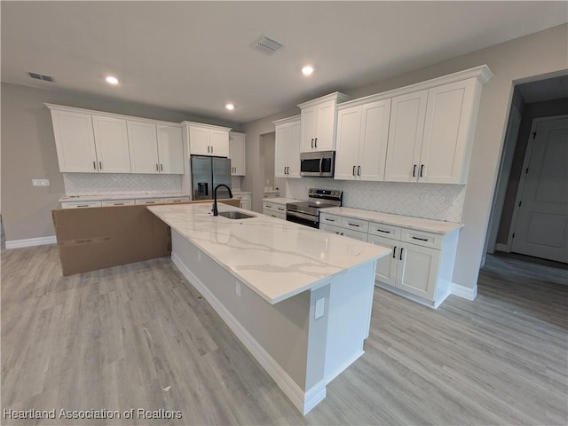 kitchen featuring appliances with stainless steel finishes, white cabinets, a kitchen island with sink, and light stone counters