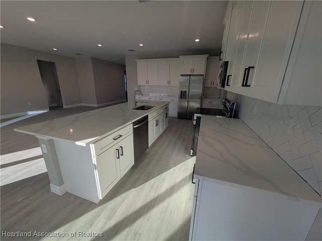 kitchen featuring light stone countertops, white cabinets, stainless steel refrigerator with ice dispenser, backsplash, and a center island with sink