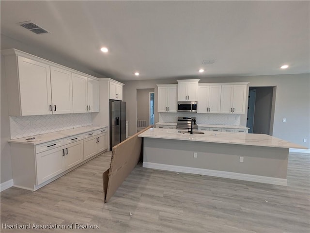 kitchen featuring sink, light stone counters, stainless steel appliances, white cabinets, and an island with sink