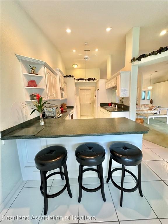 kitchen with white appliances, a kitchen breakfast bar, sink, light tile patterned flooring, and kitchen peninsula
