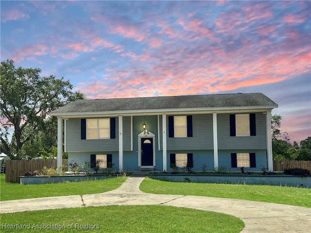 raised ranch with brick siding, fence, a yard, and covered porch