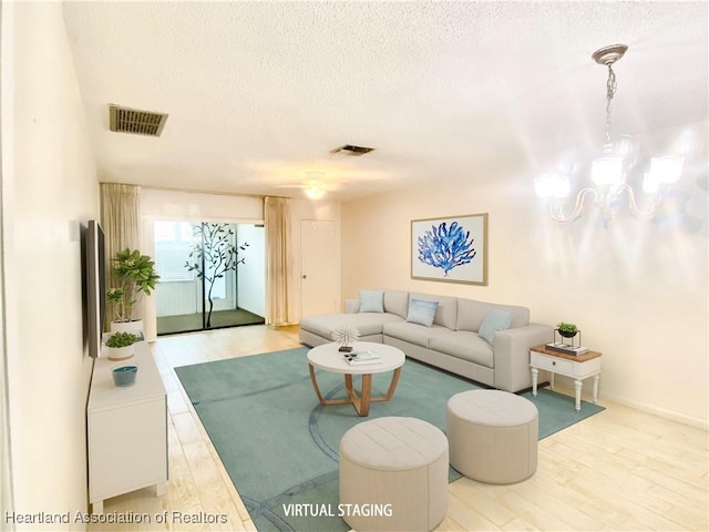 living room with light wood-style floors, a chandelier, visible vents, and a textured ceiling