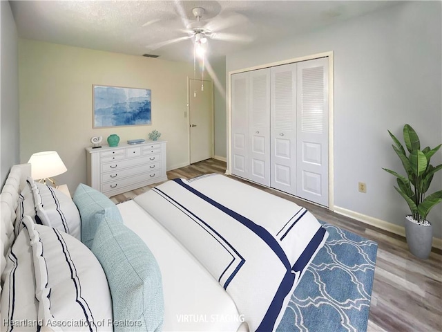 bedroom with wood finished floors, visible vents, a ceiling fan, baseboards, and a closet