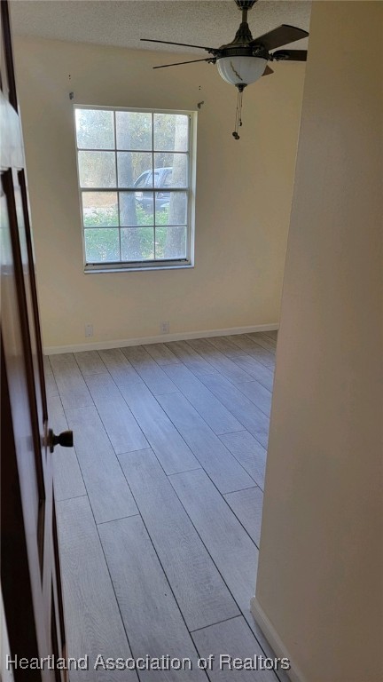 unfurnished room featuring ceiling fan, light hardwood / wood-style flooring, and a textured ceiling