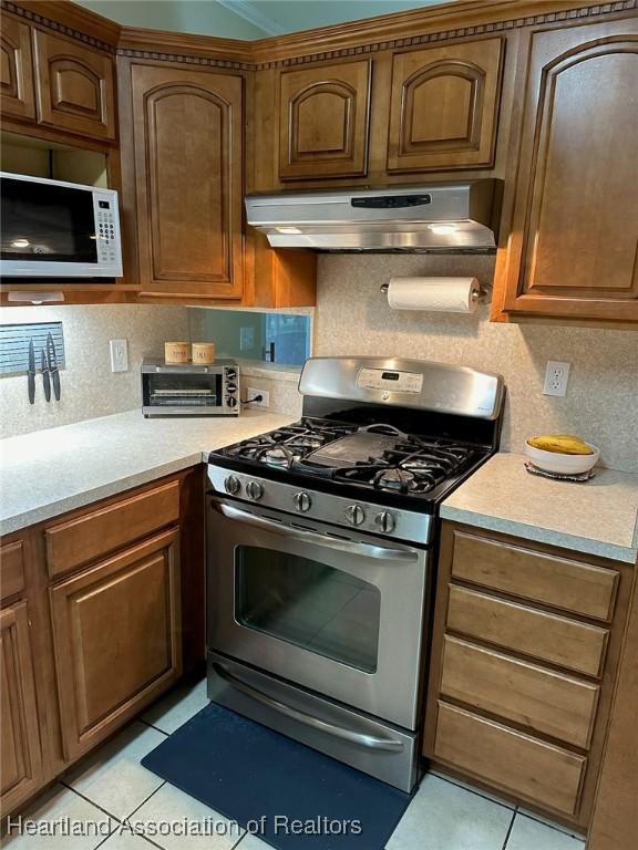 kitchen featuring decorative backsplash, gas range, and light tile patterned flooring