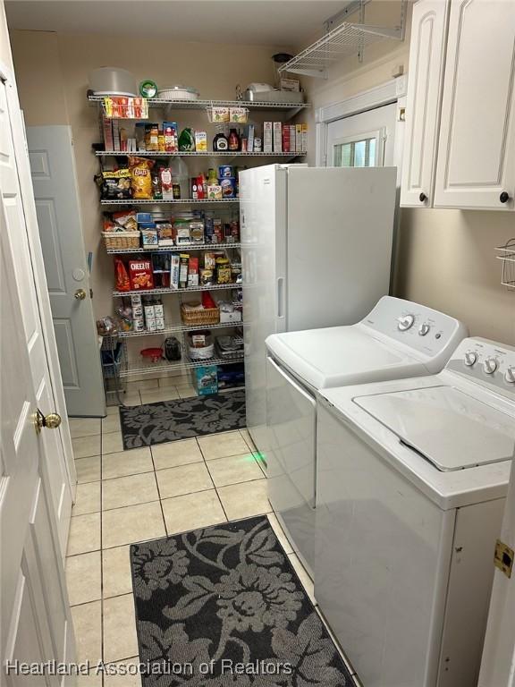 clothes washing area with light tile patterned flooring, cabinets, and washing machine and clothes dryer