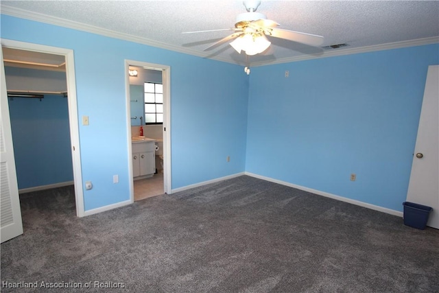 unfurnished bedroom with a walk in closet, ensuite bath, ceiling fan, crown molding, and a closet