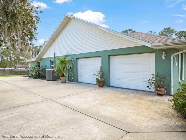 view of side of home with a garage, roof with shingles, driveway, and central AC