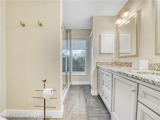 bathroom with double vanity, a stall shower, baseboards, and a sink