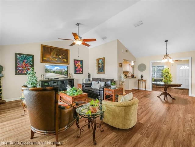 living area with vaulted ceiling, ceiling fan with notable chandelier, wood finished floors, and baseboards