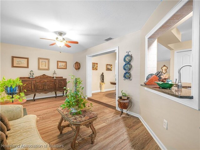 living room with a ceiling fan, baseboards, visible vents, and wood finished floors