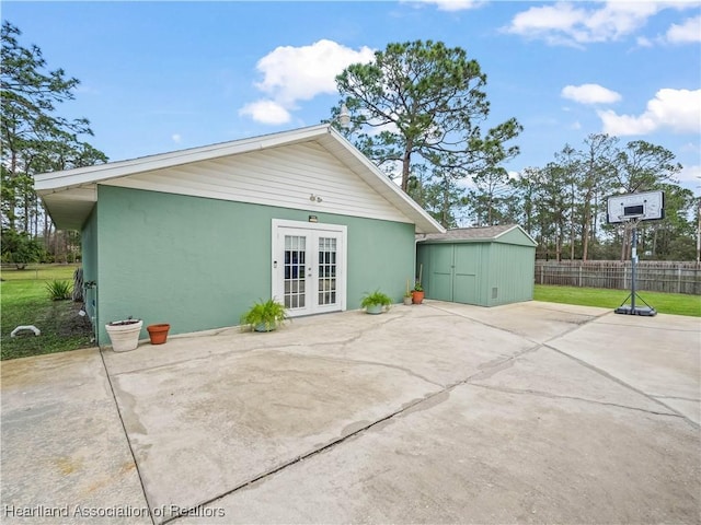 rear view of house featuring an outbuilding, french doors, stucco siding, a storage unit, and fence