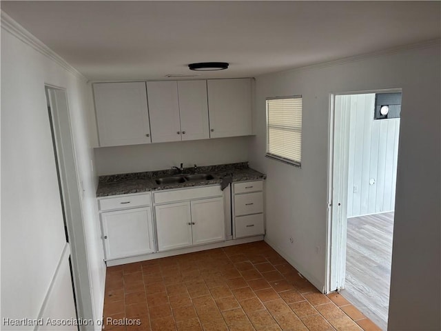 kitchen with white cabinetry, sink, dark stone countertops, and ornamental molding