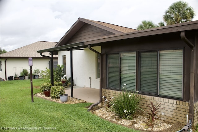 102 Oak St, Lake Placid, FL 33852 - back of property with a patio area, a lawn, stucco siding, roof with shingles, and brick siding