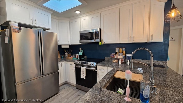 301 Sparrow Ave, Sebring, FL 33870 - kitchen featuring stainless steel appliances, a skylight, light wood-style floors, white cabinets, and dark stone counters