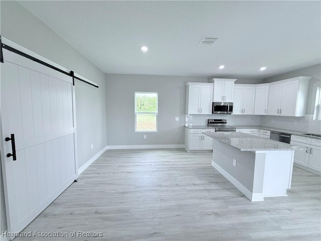 kitchen with appliances with stainless steel finishes, a barn door, a kitchen island, backsplash, and white cabinets