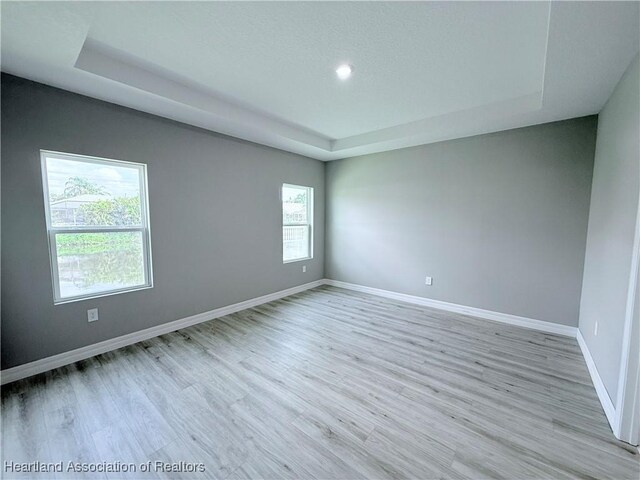 unfurnished room with a tray ceiling, light wood-style floors, baseboards, and recessed lighting