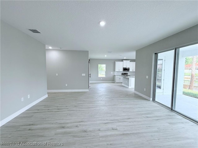 unfurnished living room with a textured ceiling, light wood-type flooring, baseboards, and recessed lighting