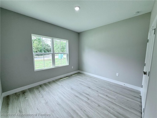 empty room featuring baseboards, light wood-style floors, a smoke detector, and a textured ceiling