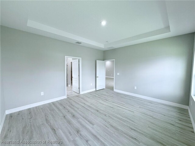 unfurnished bedroom with baseboards, light wood-type flooring, a tray ceiling, and recessed lighting