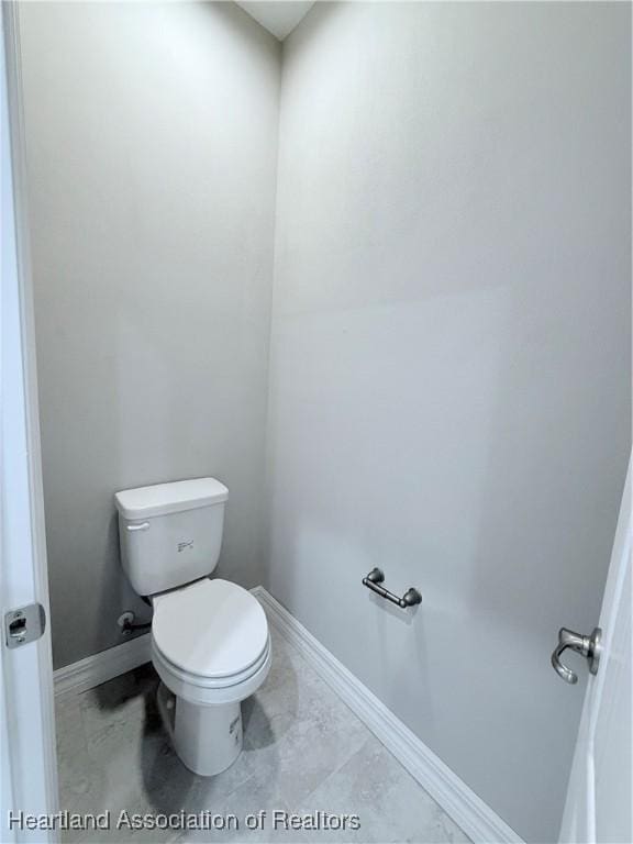 bathroom with baseboards, toilet, and marble look tiles