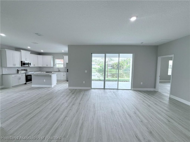 unfurnished living room featuring a sink, recessed lighting, baseboards, a textured ceiling, and light wood-style floors