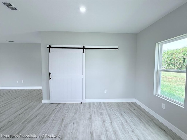 spare room with baseboards, light wood finished floors, a barn door, and recessed lighting