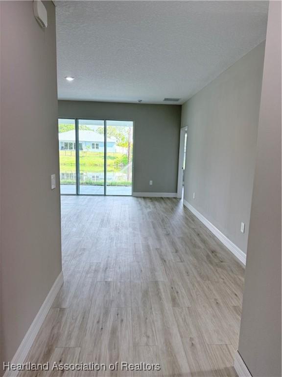 unfurnished room with a textured ceiling, baseboards, and light wood finished floors
