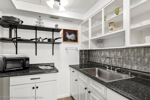 kitchen with tasteful backsplash, white cabinetry, dark stone countertops, and sink