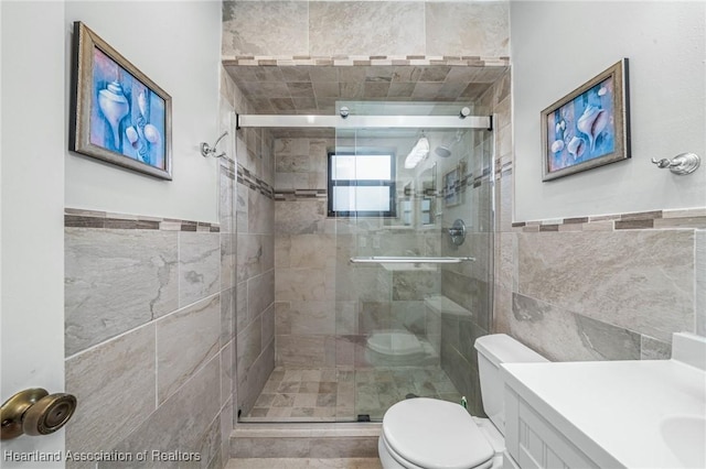 bathroom with vanity, toilet, a shower with shower door, and tile walls