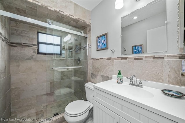 bathroom featuring vanity, toilet, a shower with shower door, and tile walls