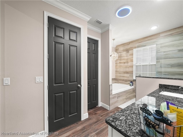 bathroom featuring hardwood / wood-style floors, vanity, a relaxing tiled tub, crown molding, and a textured ceiling