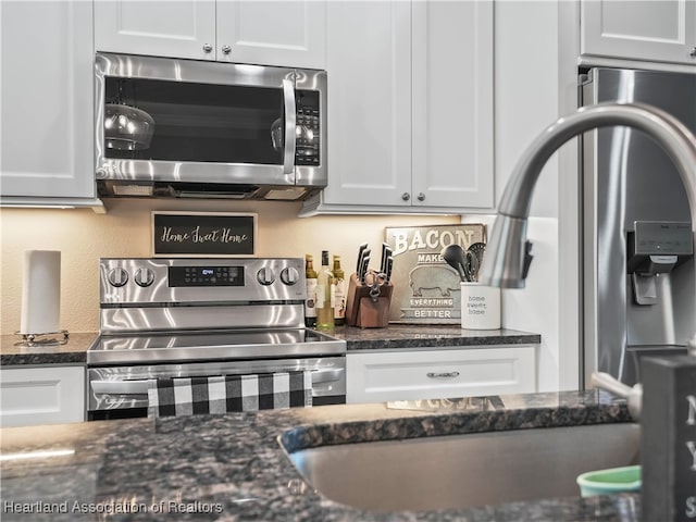 kitchen featuring dark stone countertops, stainless steel appliances, and white cabinets