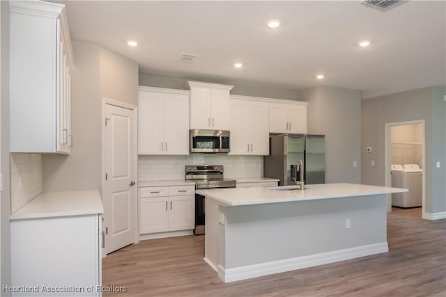 kitchen featuring appliances with stainless steel finishes, separate washer and dryer, a center island with sink, and white cabinets