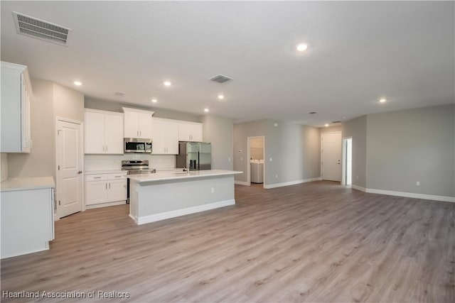 kitchen featuring washer / dryer, a center island with sink, appliances with stainless steel finishes, light hardwood / wood-style floors, and white cabinets