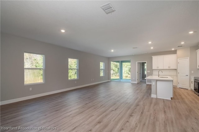 kitchen with a wealth of natural light, light hardwood / wood-style floors, an island with sink, and white cabinets