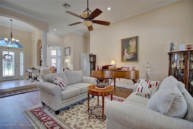 living room with ceiling fan with notable chandelier, crown molding, wood-type flooring, and decorative columns