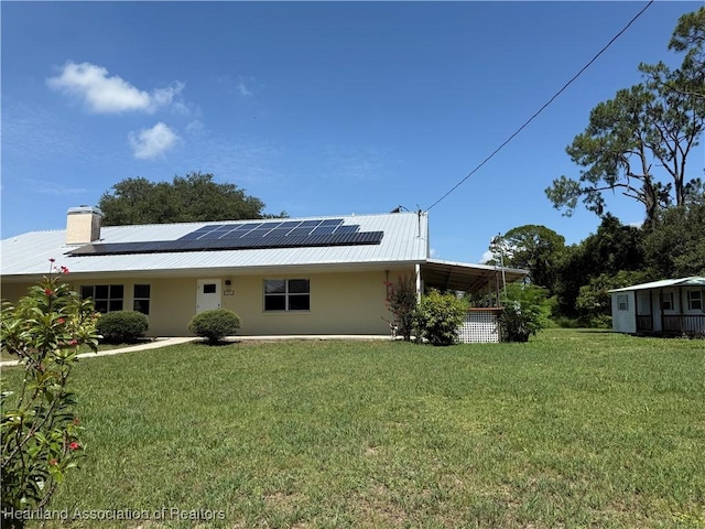 back of house with solar panels, a lawn, a metal roof, and stucco siding