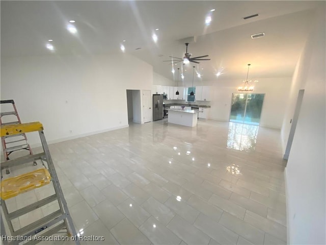 interior space featuring ceiling fan with notable chandelier, high vaulted ceiling, visible vents, and baseboards