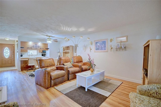 living room with ceiling fan, sink, light hardwood / wood-style floors, and a textured ceiling