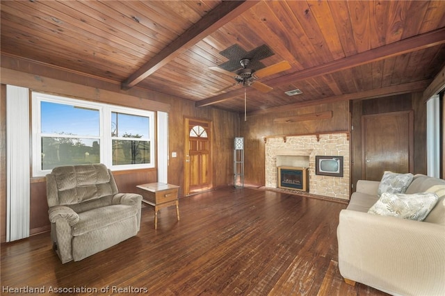 living room featuring dark wood-type flooring, a stone fireplace, wooden walls, ceiling fan, and beamed ceiling