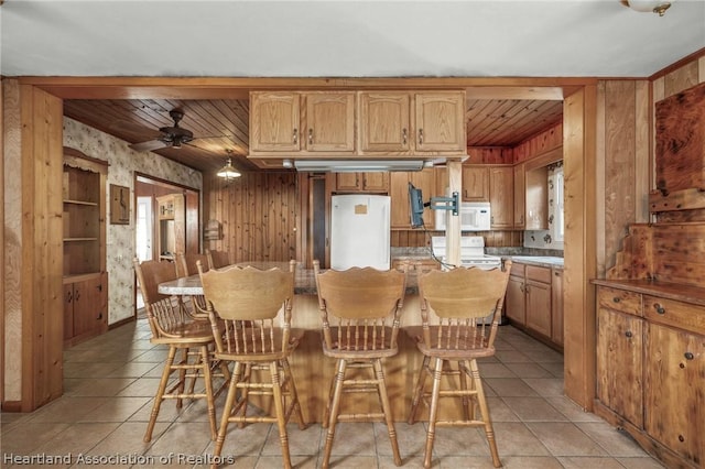 kitchen featuring a breakfast bar, white appliances, ceiling fan, light tile patterned floors, and a kitchen island