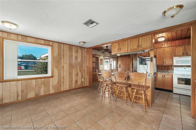 kitchen with light tile patterned floors, a kitchen bar, range, and wooden walls