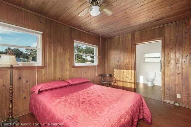 bedroom featuring wood walls, dark hardwood / wood-style floors, ceiling fan, and connected bathroom