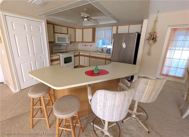 kitchen featuring visible vents, white appliances, a breakfast bar area, light countertops, and light tile patterned floors