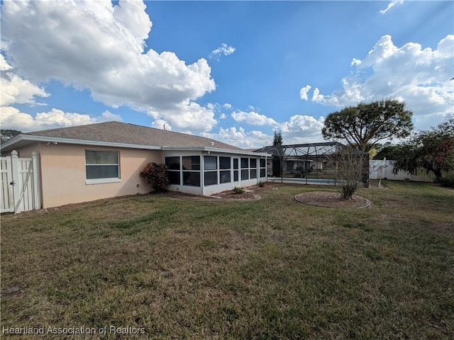 rear view of property featuring glass enclosure, fence, a lawn, and stucco siding