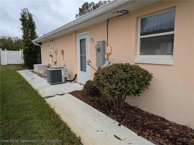 entrance to property with fence, a lawn, central AC, and stucco siding